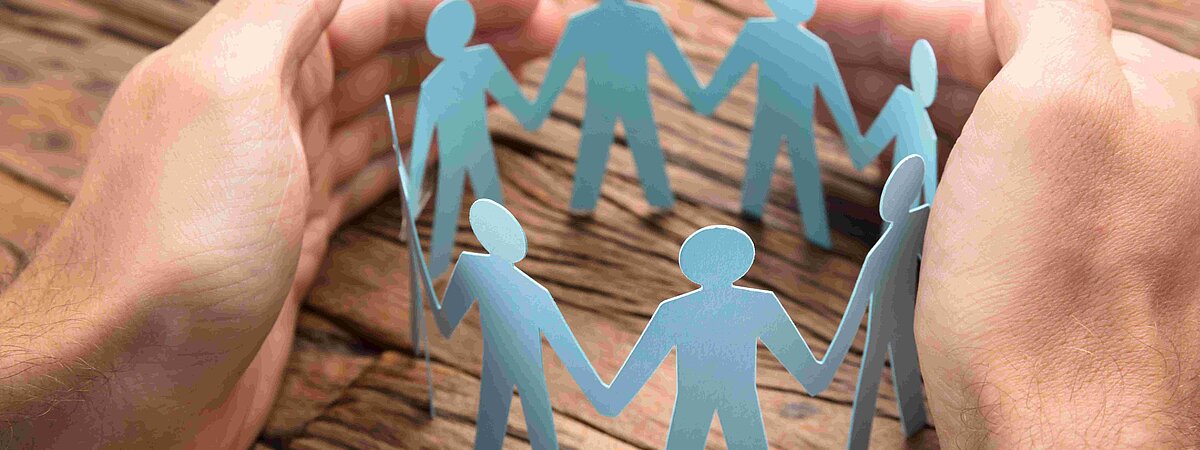 Hände umschließen eine Krone aus Pappfiguren