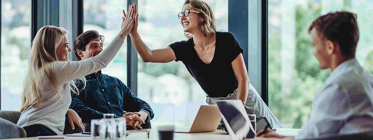 Büro mit Personen am Schreibtisch_Handschlag über den Tisch hinweg